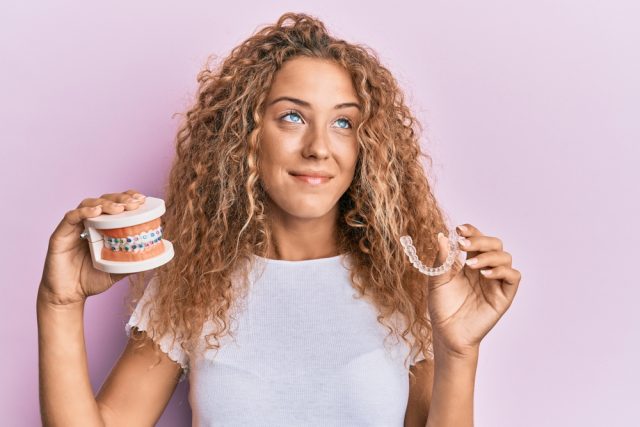 girl holding a clear aligner and model of teeth with braces