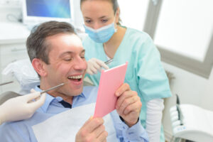 man smiling into hand mirror at dental office