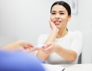woman holding cheek in pain talking to dentist